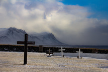 Cemetery in Iceland with several cross grave markers and dramatic mountains, clouds and sea in background