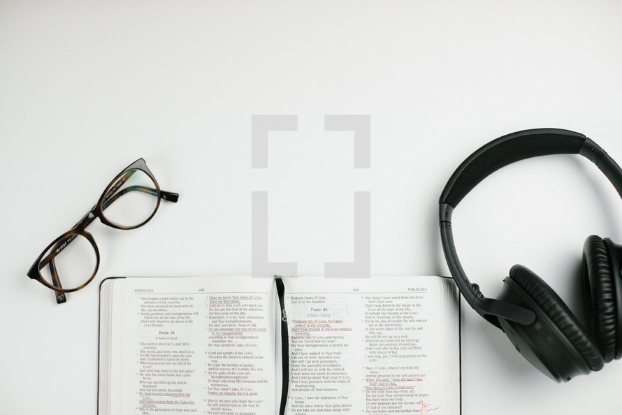 reading glasses, open Bible, and headphones on a white desk 
