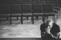Man leaning on stage with eyes closed in prayer.