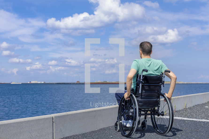 Disabled man in a wheelchair admiring the sea. Travel, mobility and freedom concept.