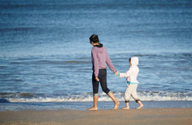 mother and daughter walking barefoot on a beach 
