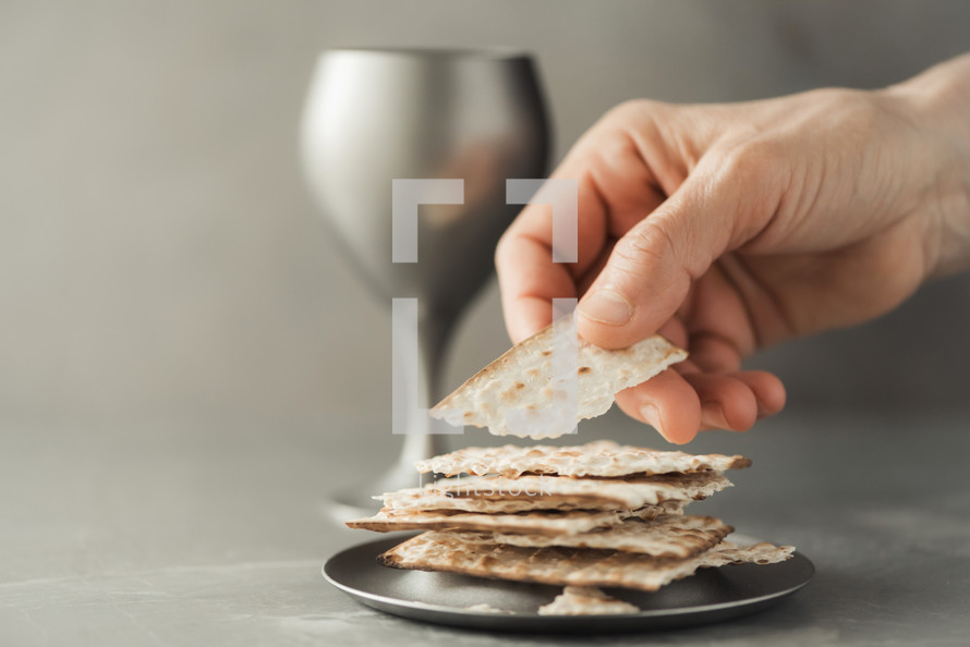 Hands with chalice and communion matzo bread, wooden cross on grey background. Christian communion for reminder of Jesus sacrifice. Easter passover. Eucharist concept. Christianity symbol and faith