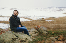 a man sitting on a rock in front of a snow covered landscape 