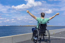 Disabled man in a wheelchair admiring the sea. Travel, mobility and freedom concept.