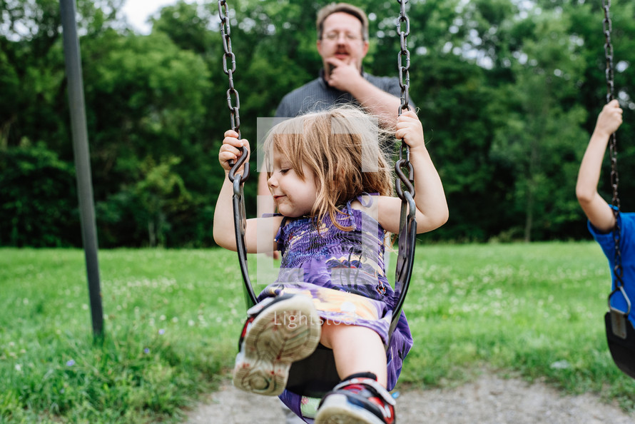 father pushing his daughter on a swing 