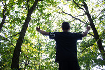 boy standing outdoors in a forest with hands raised 