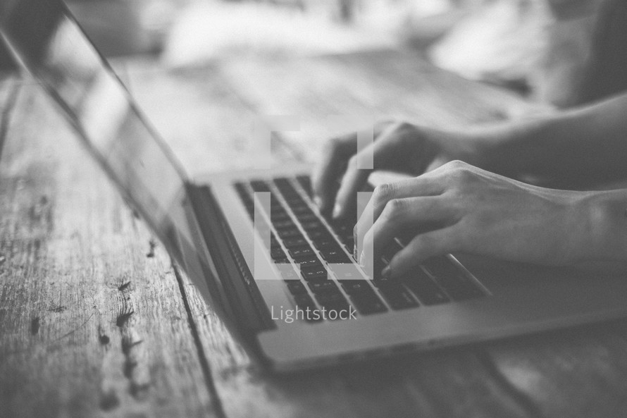 Hands typing on a laptop on a wooden table.
