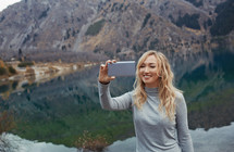 a woman taking a selfie standing in front of a lake 