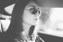 a woman driving a car wearing sunglasses 