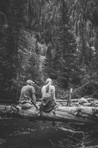 man and woman sitting on a fallen tree outdoors 