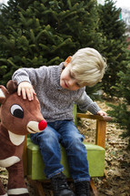 a boy child petting a stuffed Rudolph in a Christmas tree farm 