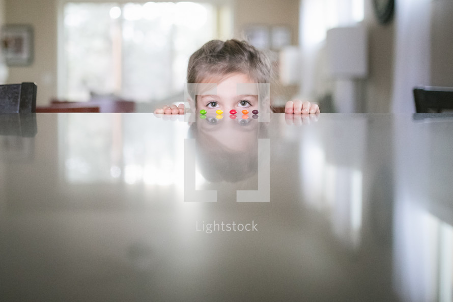 a girl child peeking over a countertop at candy