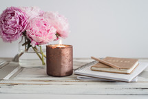 peonies, votive candle, and journals on a table 