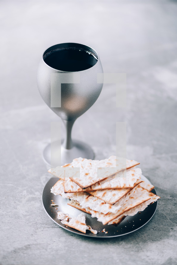 Communion still life. Unleavened bread, chalice of wine, silver kiddush wine cup on grey background. Christian communion concept for reminder of Jesus sacrifice. Easter passover