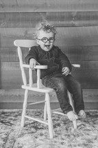 a toddler in glasses sitting in a chair 