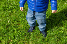 Close-up of a young child in blue taking tentative steps outdoors on vibrant green grass