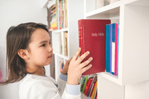 Little girl taking the bible from her library