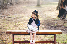 a little girl sitting on a bench reading a Bible 