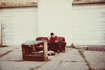 man sitting on a old couch in front of an old entertainment center outdoors