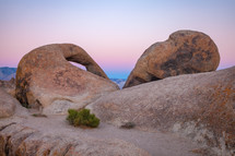 Natural stone Arch near Alabama Hills California with ombre sky background and plant growing in sand  