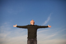 elderly man standing outdoors with his arms outstretched in worship to God
