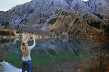 a woman taking a picture of a lake with her cellphone 