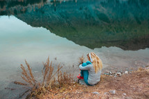 girl listening to headphones sitting by the edge of a pond 