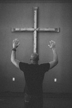 man with his arms raised in praise and worship to God standing in front of a cross