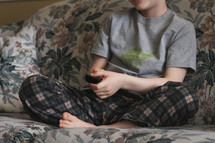 boy sitting on a couch with a remote control 