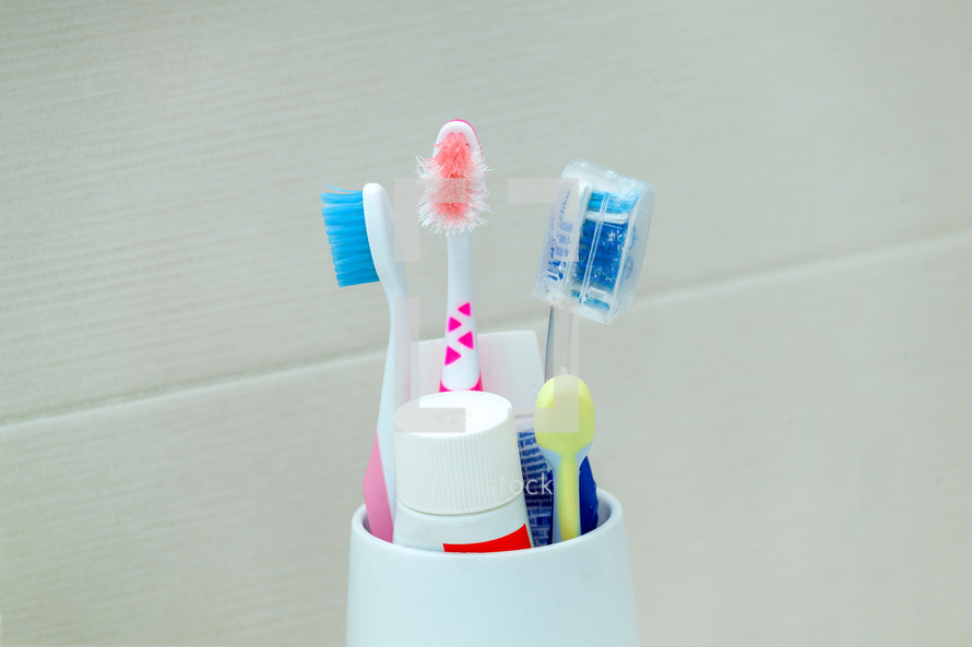 Used and ruined toothbrushes in a white holder on a neutral background.
