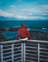 a man in a red coat looking out at the ocean 