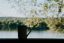 A coffee cup is silhouetted in front of a lake in northern Ontario. A peaceful moment for prayers and meditation.