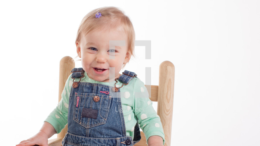 toddler girl in overhauls sitting in a chair 