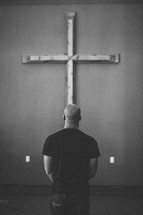 man standing in prayer in front of a cross