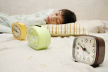 Sleeping boy at the morning and three alarm-clocks