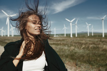 woman with hair blowing standing in a front of a wind farm