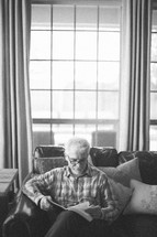elderly man sitting on a couch reading a Bible