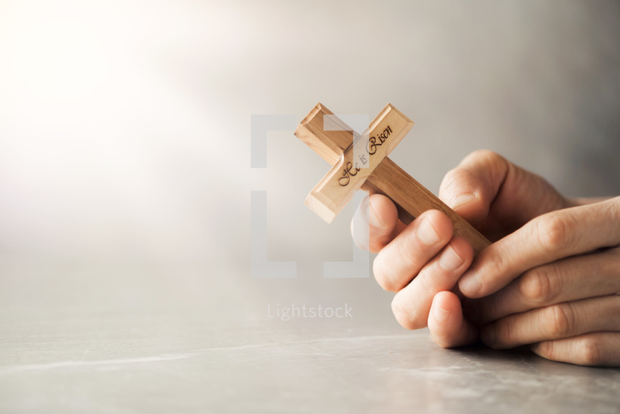 Wooden cross with text "He is risen" on grey background.