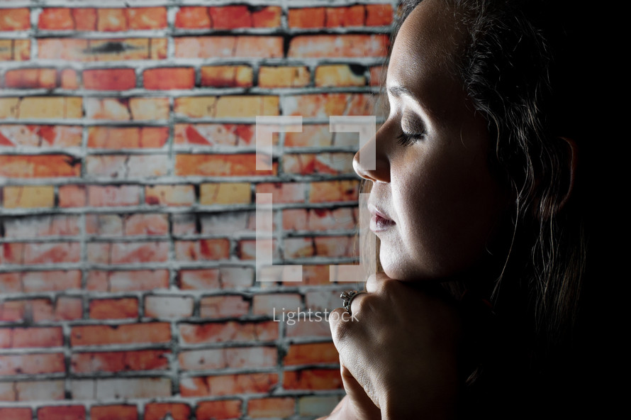 woman in prayer and a brick wall 