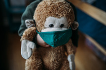 toddler hugging a stuffed animal monkey wearing a face mask 