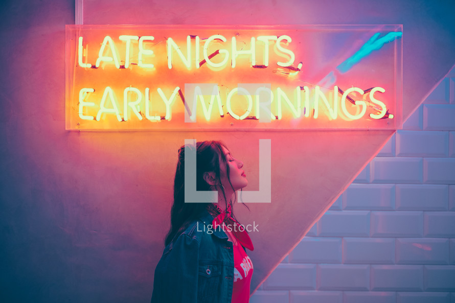 Late Nights, Early Mornings neon sign and a woman standing under it 
