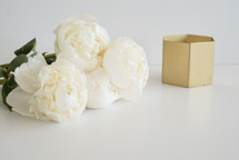White flowers and a gold box on a white surface.