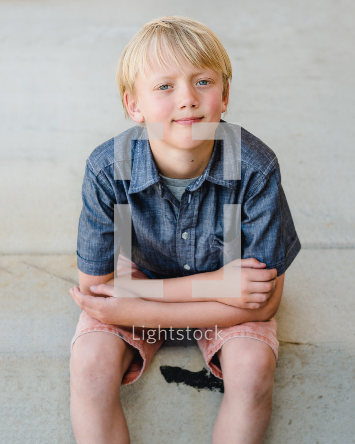 portrait of a young boy sitting on a curb 