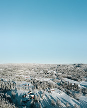 Aerial photo of a farm surrounded by snow covered trees.