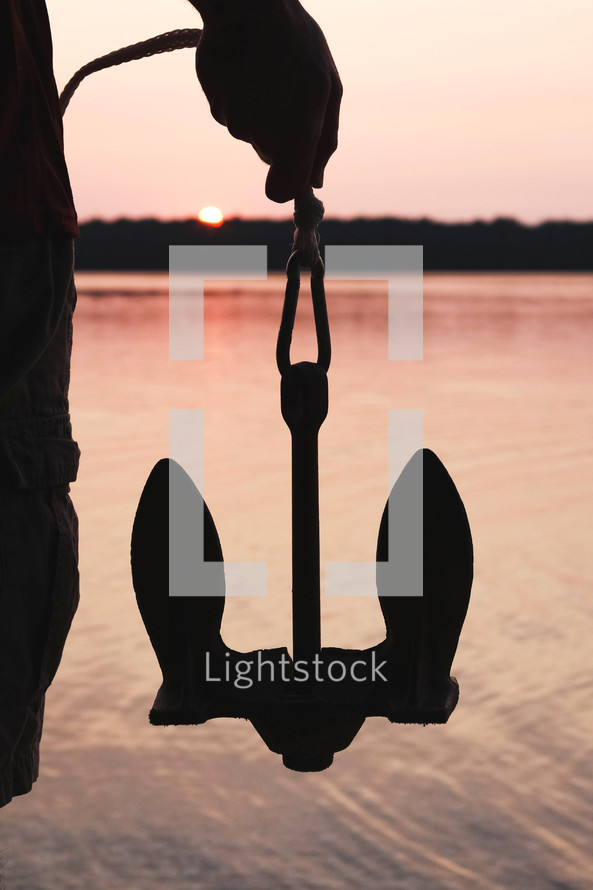 a man holding an anchor at sunset 