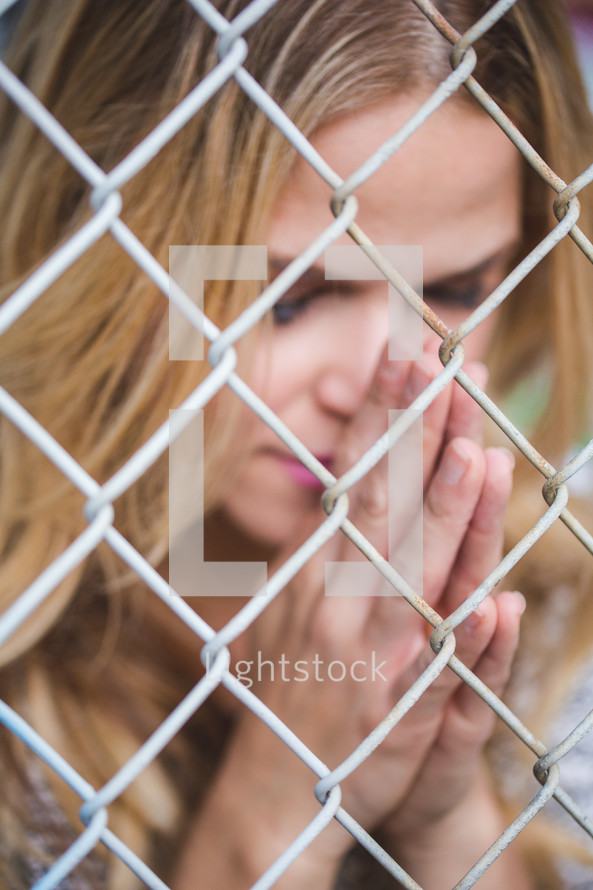 a woman clinging to a chain link fence with praying hands 