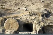 An open tomb in the side of a hill with a circular stone nearby.