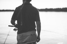 a man holding a fishing pole at a lake 