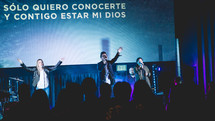 Performers on stage in front of Spanish lyrics on a projection screen 
