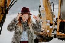 a woman in a fur coat standing under a backhoe in snow 